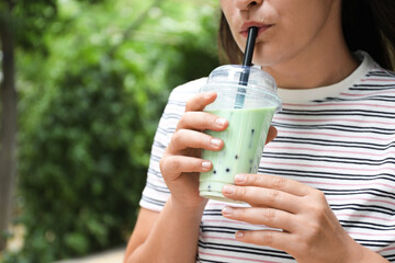 Woman drinking tasty milk bubble tea from plastic cup outdoors, closeup. Space for text