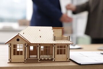 Real estate agent giving key to client at desk in office, focus on house model