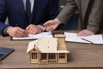 Real estate agent working with client at desk in office, focus on house model