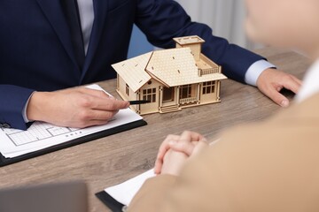 Real estate agent working with client at desk with house model in office, closeup