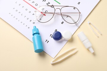Vision test chart, glasses, tweezers, lenses and bottles of medical drops on beige background, flat...