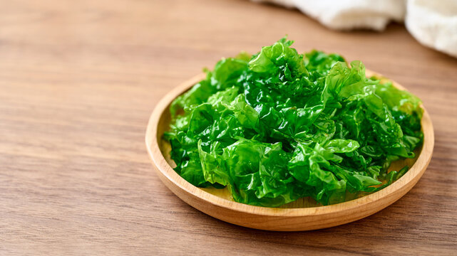 closeup heap of green laver ulva lactuca or sea lettuce seaweed in wooden bowl on wood table food background with copy space