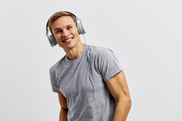 Smiling young man with short blond hair wearing gray t-shirt listening to headphones and looking at...