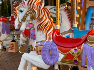 Brightly painted carousel horses stand ready at an amusement park, illuminated by warm afternoon...