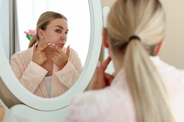 Woman with acne problem looking in mirror at home