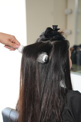 Naklejka premium Hairdresser Holding Round Brush Behind Woman’s Back During Hair Blow-Dry