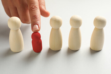 Dismissal. Woman choosing red figure among wooden ones at white table, closeup