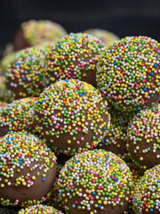 chocolate candies in colorful sprinkles close-up, sweet dessert background