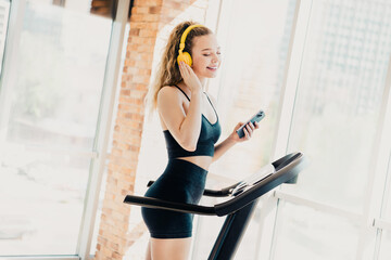 Young woman exercising on treadmill while listening to music on headphones in a stylish indoor gym...