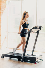 Athletic active woman exercising on a modern treadmill in a bright interior gym, practicing healthy...