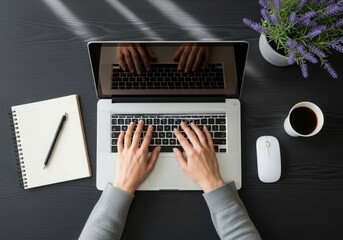 Overhead view of a person typing on a laptop with coffee and notebook