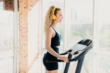 Athletic woman exercising on a treadmill indoors wearing headphones, focusing on fitness and...