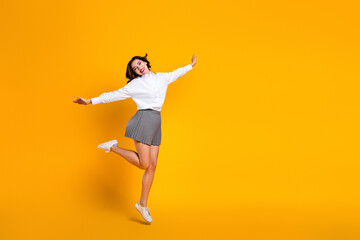 Obraz premium Cheerful brunette woman posing joyfully in stylish outfit on vibrant yellow background with playful expression