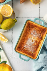 Baked lemon pudding with lemon zest and juice garnished with powdered sugar in blue baking dish on...