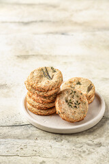 Shortbread cheese cookies with aromatic herbs on white plate on rustic textured background isolated. Savory parmesan cookies for party