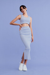 young woman in light blue sleeveless crop top and matching skirt stands confidently against pastel...