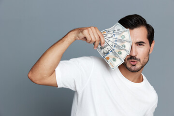 Confident man holding cash bills close to face, looking at camera with playful expression....