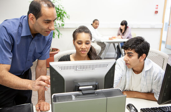 Computer Studies; Technology Tutor. A teacher helping a pair of late-teenage students in the classroom. From a series of related images. - Powered by Adobe