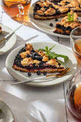 A slice of homemade blueberry crumble pie on a plate on white tile background. Sweet breakfast composition in bright morning light