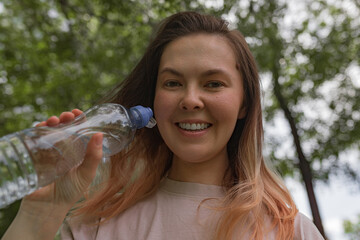 Woman smiling directly at camera holding clear sport water bottle with blue cap wearing pale shirt...