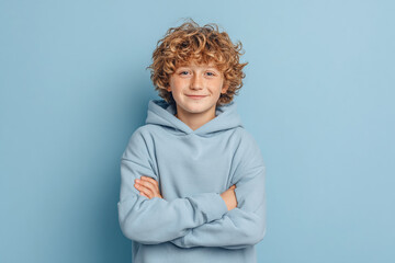 Smiling boy stands arms crossed against blue. Portrait showcases kid's self-assuredness. Use for ads, web content, design projects, and educational materials.