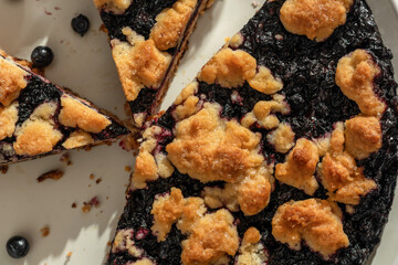 Sliced homemade blueberry crumble pie on a plate close up top view. Sweet breakfast composition in bright morning light