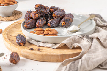 Medjool dates and almonds on a wooden tray with a spoonful of sugar, showcasing a healthy snack option