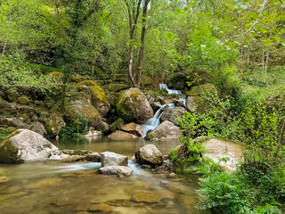 Barrias Waterfall Serenity. A gentle waterfall cascades over moss-covered rocks into a calm, clear...