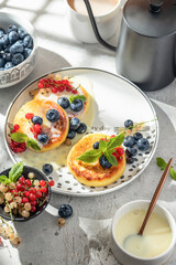 Cottage cheese pancakes with berries and condensed milk. Homemade dessert syrniki for healthy breakfast, bright morning light