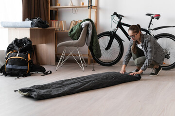 Female Backpacker in eyeglasses rolling sleeping bag for camping, packing for her trip at home...