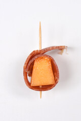 A single appetizer, featuring a vibrant orange melon cube wrapped in prosciutto and secured with a...
