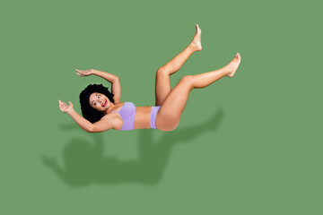Confident woman in purple lingerie posing gracefully against a green background, celebrating body...