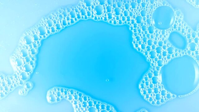 Top down slow zoom shot of clean soap foam bubbles on a light blue liquid background