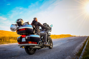Fototapeta premium A person on a touring motorcycle riding into the sunrise on a rural road. Concept of freedom, solitude, and adventure on the open road. Space for copy on the right side.