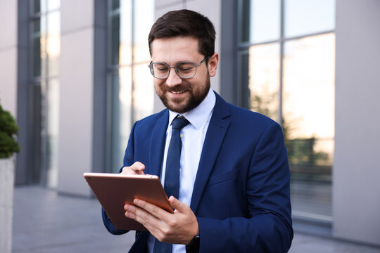 Successful businessman with tablet near office building