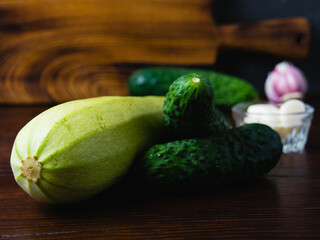 Green vegetables on a dark background. Cucumbers, garlic and zucchini on a wooden table. Concept of cooking healthy food and healthy eating