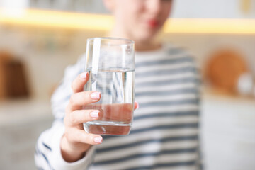 Woman with glass of water in kitchen, closeup