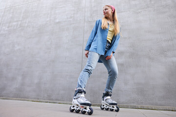 Beautiful young woman with roller skates near gray wall outdoors, low angle view