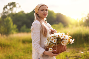 Happy woman with basket full of beautiful wildflowers outdoors