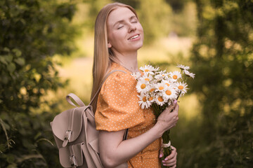 Beautiful woman with bouquet of wildflowers and backpack in forest