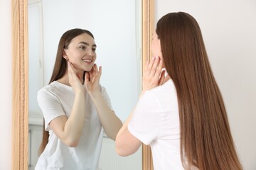 Beautiful woman looking at herself in mirror indoors