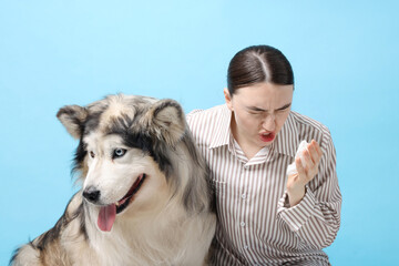 Woman suffering from allergy with her dog on light blue background