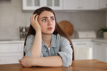 Fototapeta premium Scared woman suffering from paranoia at table in kitchen