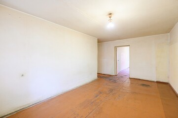 empty room with beige walls, a worn wooden floor, and a simple light fixture. An open doorway leads to another room