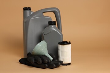 Motor oil in plastic canisters, filter, gloves and funnel on beige background, space for text