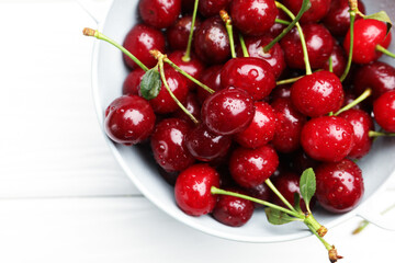 Fresh wet cherries in colander on white wooden table, top view