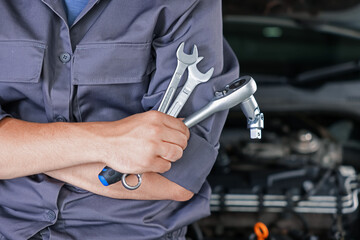 Auto parts. Professional mechanic with different wrenches near open hood of car indoors, closeup....