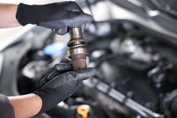 Auto part. Professional mechanic with drive shaft near open hood of car indoors, closeup. Space for...