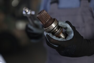Auto part. Professional mechanic with drive shaft and tool indoors, closeup. Space for text