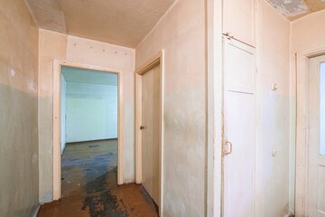 interior shot of a worn hallway with doorways, old paint, and aged wooden floors. The space suggests a need for renovation